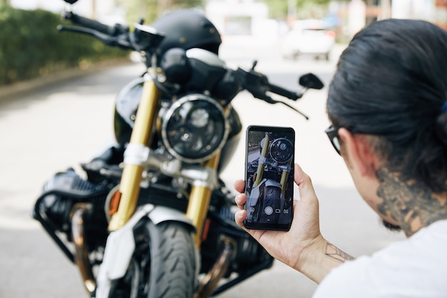 Mann macht coole Fotos von seinem Motorrad auf dem Smartphone, um sie mit Freunden zu teilen oder in sozialen Medien zu posten