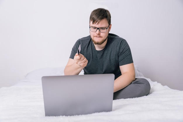 Mann macht Internet-Shopping auf seinem Laptop, während er auf dem Bett sitzt