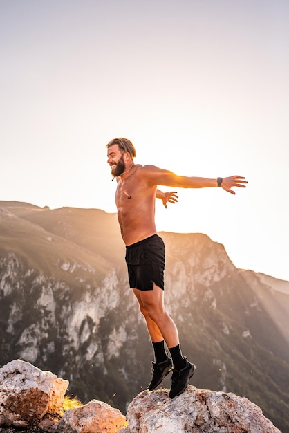 Mann macht Konditionstraining auf einem Berggipfel am frühen Morgen mit dem Sonnenaufgang im Hintergrund