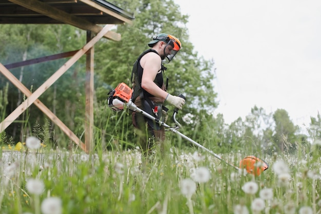 Mann mäht hohes Gras mit Benzin-Rasentrimmer im Garten oder Hinterhof Prozess des Rasentrimmens mit Handmäher