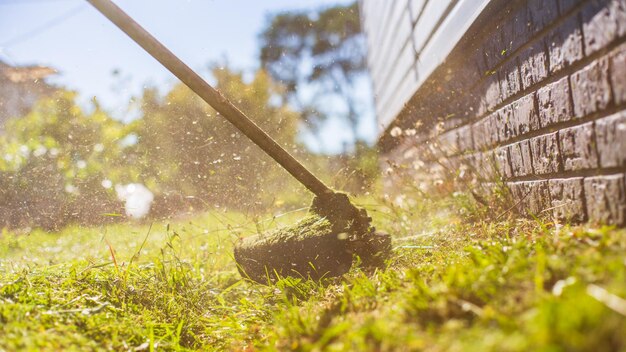 Mann mäht hohes Gras mit elektrischem oder Benzin-Rasentrimmer im Hinterhof Gartengeräte und -ausrüstung Prozess des Rasentrimmens mit Handmäher