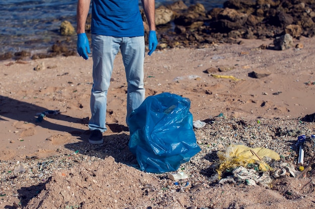 Mann meldet sich freiwillig mit großer Tasche für Müll, der Müll am Strand sammelt. Konzept der Umweltverschmutzung