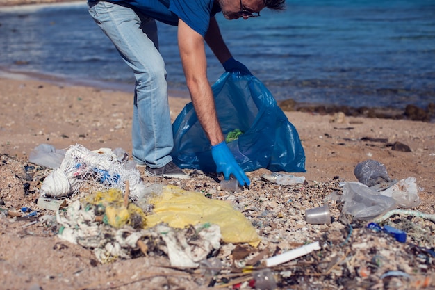 Mann meldet sich freiwillig mit großer Tasche für Müll, der Müll am Strand sammelt. Konzept der Umweltverschmutzung