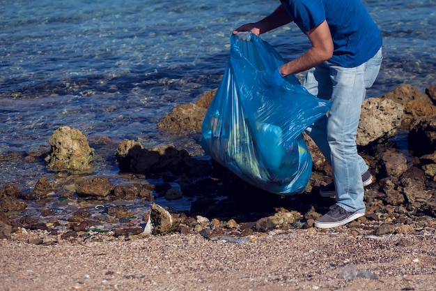 Mann meldet sich freiwillig mit großer Tasche für Müll, der Müll am Strand sammelt. Konzept der Umweltverschmutzung