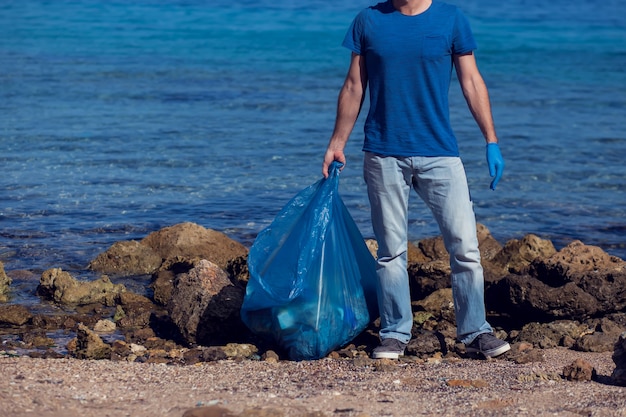 Mann meldet sich freiwillig mit großer Tasche für Müll, der Müll am Strand sammelt. Konzept der Umweltverschmutzung