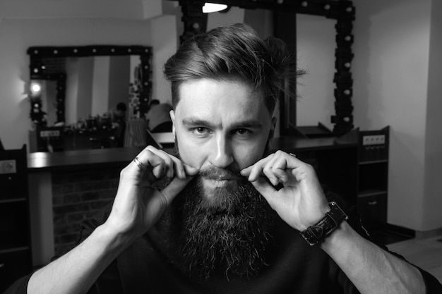 Mann mit Bart, der seine Schnurrbärte im Stehen vor grauem Hintergrund anpasst