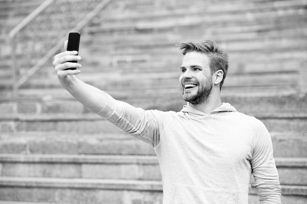 Mann mit Bart geht mit Smartphone urbaner Hintergrund mit Treppe Mann Blogger mit Videokonferenzen auf dem Smartphone Blogger-Konzept Blogger nutzen Smartphones, um Videos online zu streamen