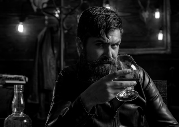 Mann mit Bart hält Glasbrandy-Macho-Trinkverkostung, die einen hübschen, stilvollen bärtigen Mann co