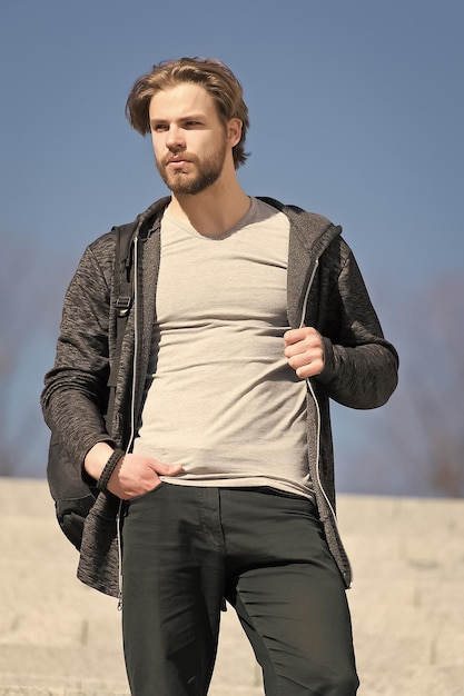 Mann mit Bart in Freizeitkleidung auf sonniger Outdoor-Mode Macho-Stand auf blauer Himmelsperspektive Perspektive zukünftige Freiheit Herrenmode und -stil