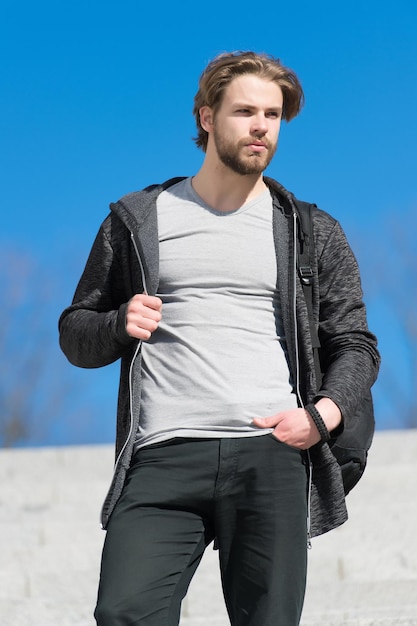 Mann mit Bart in Freizeitkleidung im sonnigen Outdoor, Mode. Macho-Stand auf blauem Himmel, Perspektive. Perspektive, Zukunft, Freiheit. Herrenmode und Stil