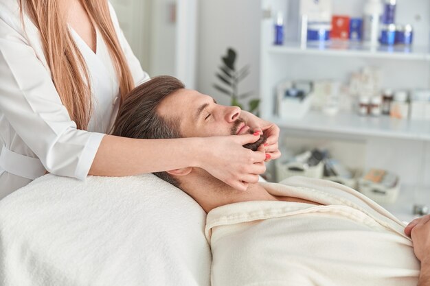 Mann mit bart liegt auf dem rücken und bekommt eine facelifting-massage. gesichtsmassage schönheitsbehandlung. wellness-, beauty- und entspannungskonzept.