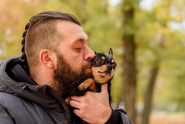 Mann mit Bart und Chihuahua. Ein Mann im Park mit seinem geliebten Haustier im Arm. Kerl mit Hund