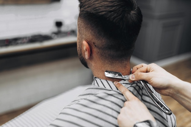 Mann mit Bartkunde im Friseursalon beim Rasieren mit gefährlichem Rasiermesser