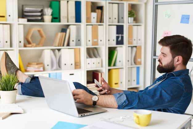 Mann mit Beinen auf Schreibtisch im Büro