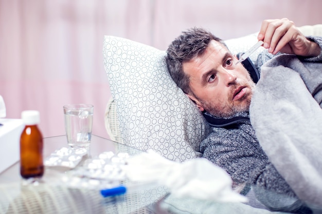 Foto mann mit blauem schal bekam grippe und temperaturmessung. konzept für menschen, gesundheitswesen und medizin