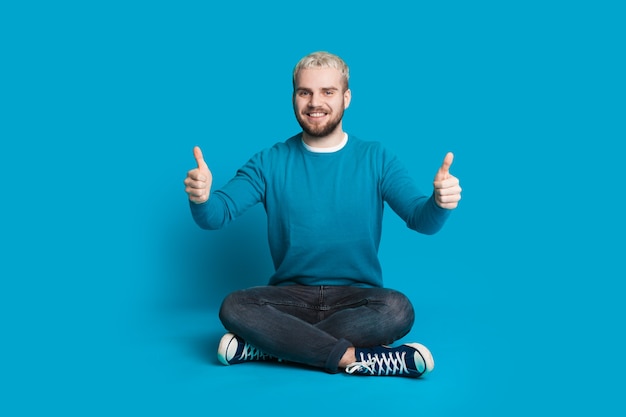 Mann mit blonden Haaren sitzt, während er das gleiche Zeichen gestikuliert