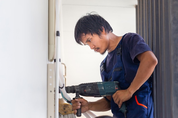 Mann mit Bohrhammer, der ein Loch in der Wand macht Technikermann, der eine Klimaanlage in einem Kundenhaus installiert Junger Mechaniker, der die Klimaanlage repariert Wartungs- und Reparaturkonzepte