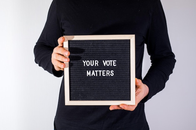 Mann mit Briefbrett mit Text Your Vote Matters auf weißem Hintergrund