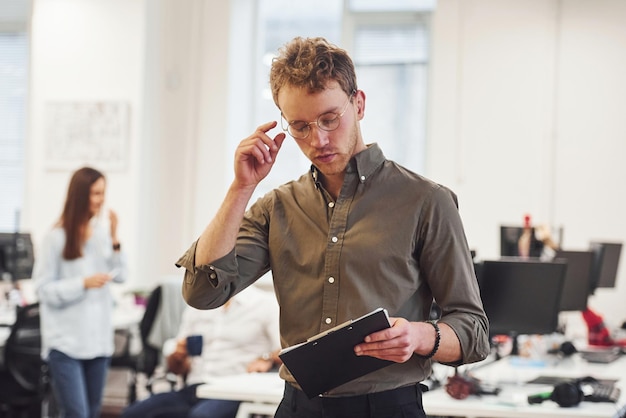 Mann mit brille, der vor geschäftsleuten steht, die im modernen büro zusammenarbeiten.