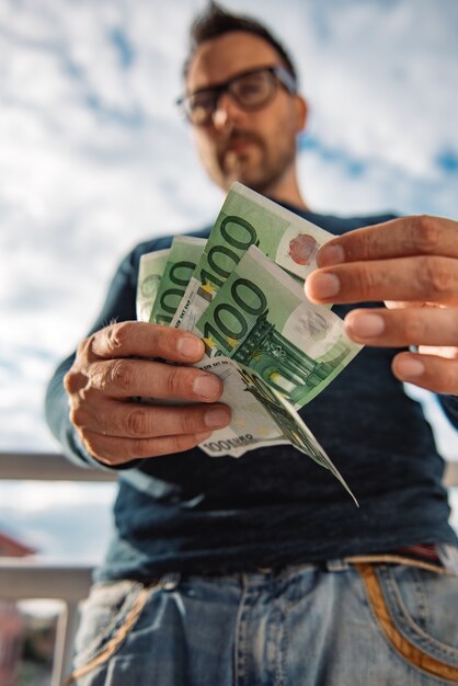 Mann mit Brille trägt blaues Hemd. und hält einen Stapel Geld.