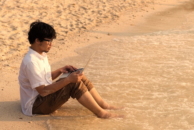 Mann mit Computer am Strand. an Computer draußen arbeiten beim Reisen, Freiberuflerkonzept.