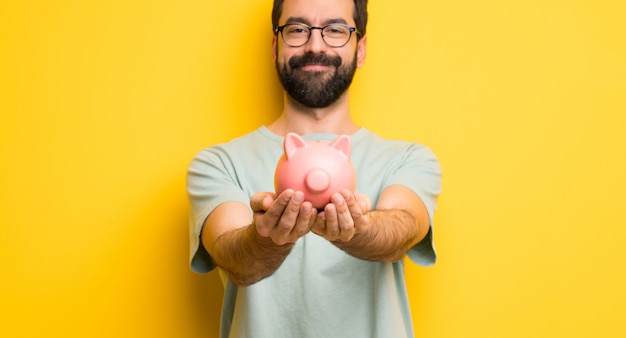 Mann mit dem Bart und grünem Hemd, die ein piggybank halten