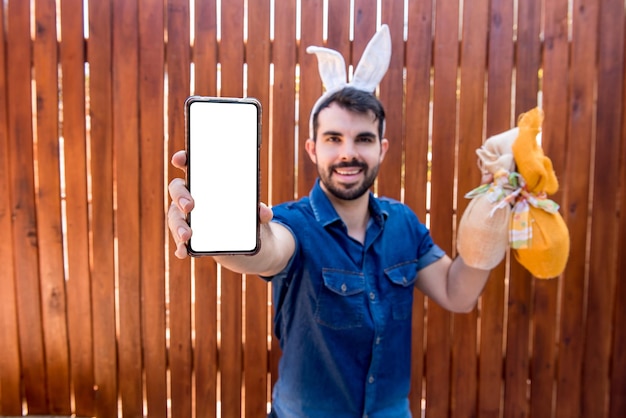 Mann mit dem Osterhasenohr, das Handy und Ostereier selektiven Fokus hält