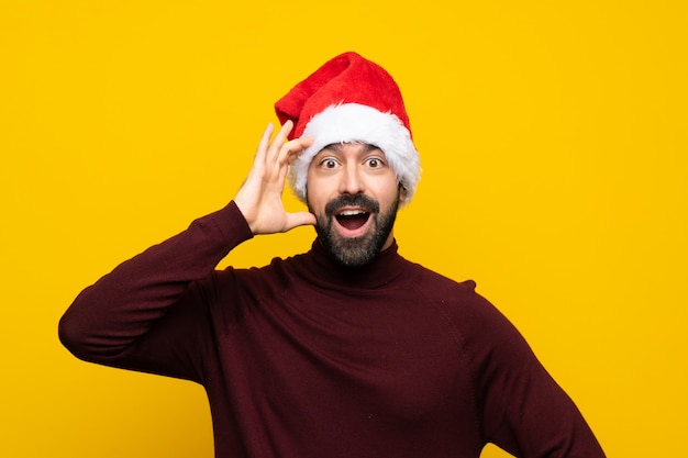 Mann mit dem Weihnachtshut, der Überraschungsgeste über lokalisiertem gelbem Hintergrund tut