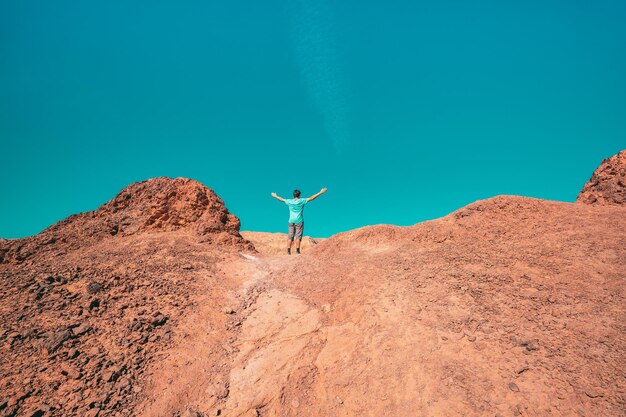 Mann mit den Händen in der Luft, der auf einem Felsen in der Wüste steht