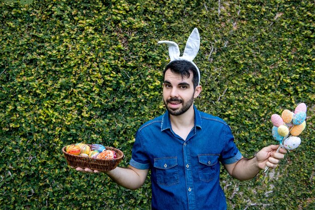 Mann mit den Osterhasenohren, die farbige Ostereier halten