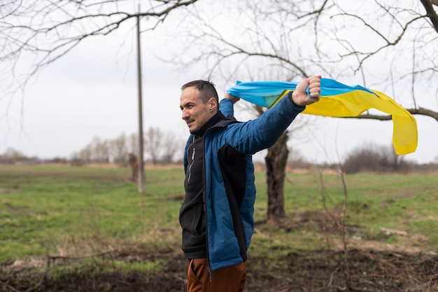 Mann mit der Flagge der Ukraine nahe dem verbrannten Baum