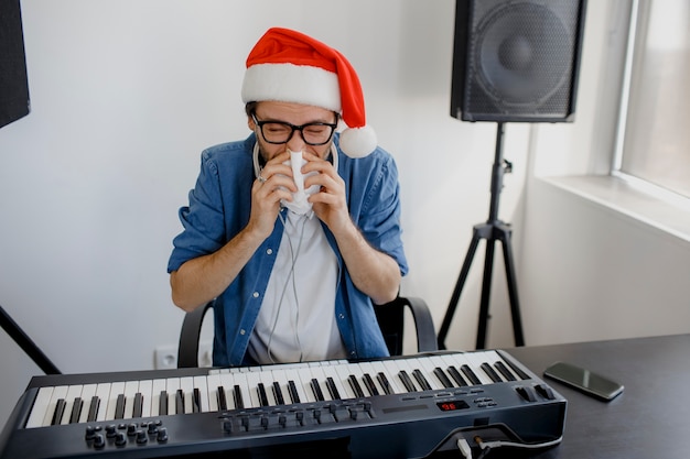 Mann mit der Weihnachtsmütze, die Klavier spielt und seine Nase putzt