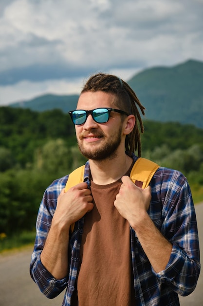 Mann mit Dreadlocks und Bart reist mit Rucksack durch die Berge, gutaussehend und selbstbewusst