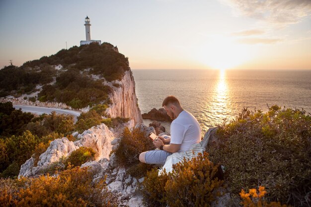 Mann mit Drohne an der Klippe bei Sonnenuntergang über dem Leuchtturm