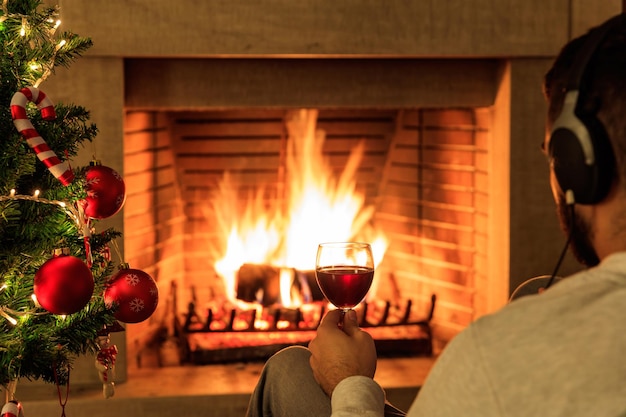 Mann mit einem Glas Rotwein am Weihnachtsbaum und brennendem Kaminhintergrund