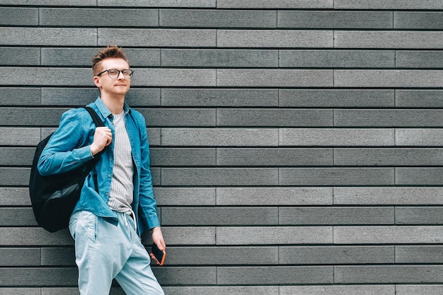 Mann mit einem Rucksack, der ein Smartphone in der Hand hält, während er auf dem Hintergrund einer grauen Wand steht