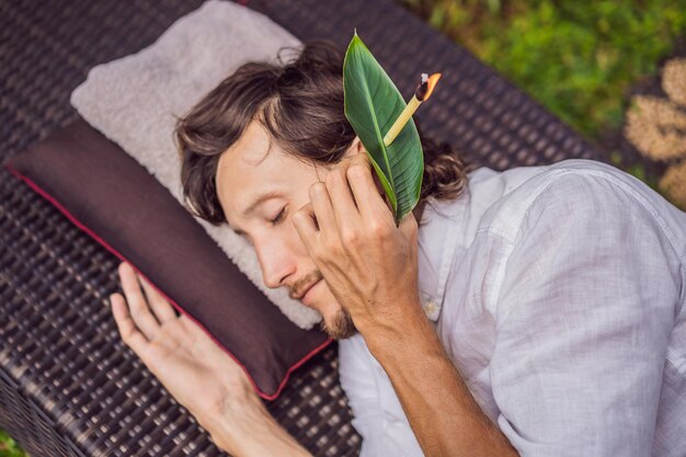 Mann mit einer Ohrkerzentherapie vor dem Hintergrund eines tropischen Gartens