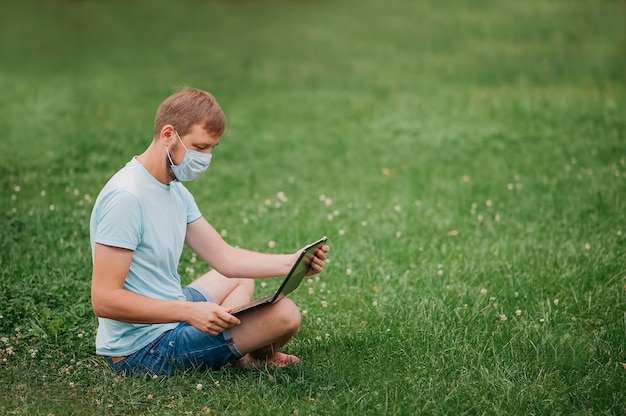 Mann mit einer Schutzmaske unter Verwendung eines Laptops in der Natur