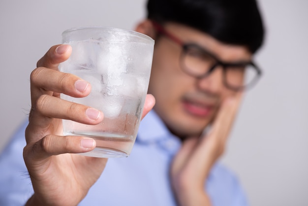 Mann mit empfindlichen Zähnen und hält Glas kaltes Wasser mit Eis