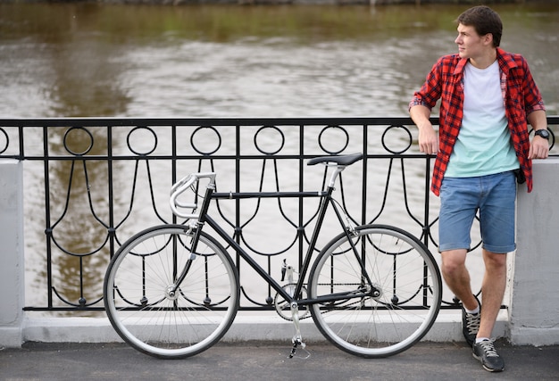 Mann mit Fahrrad, das auf Brücke ruht