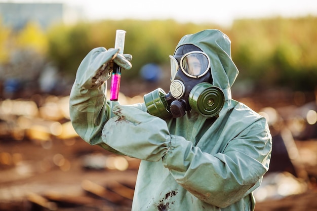 Mann mit Gasmaske und grüner Militärkleidung erkundet Fässer nach Chemiekatastrophe