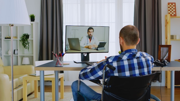 Mann mit Gehbehinderung im Rollstuhl, der mit seinem Arzt per Videoanruf spricht.