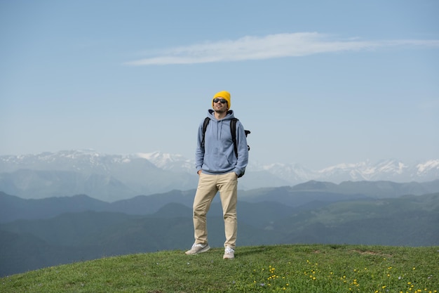 Mann mit gelbem Hut und blauem Kapuzenpullover bestieg den Gipfel gegen die schneebedeckten Berggipfel