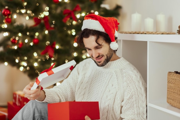 Mann mit Geschenk in der Geschenkbox in der Nähe des Weihnachtsbaums zu Hause