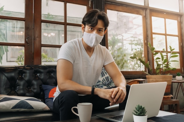 Mann mit Gesichtsmaske arbeitet mit Laptop in einem Café