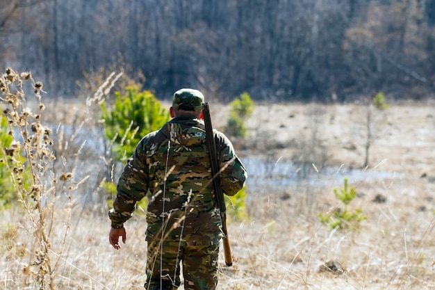 Mann mit Gewehr in Tarnkleidung geht in den Wald