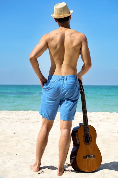 Mann mit Gitarre am Strand mit dem Meer als Hintergrund.