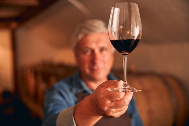 Mann mit Glas alkoholischem Getränk in der Hand, der im Weinkeller steht