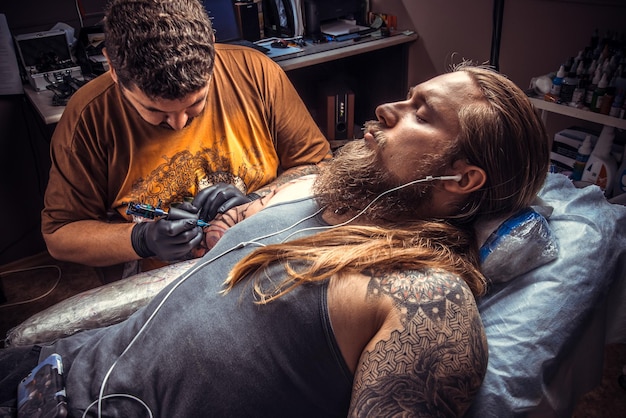 Mann mit Handschuhen, der den Prozess der Tätowierung im Tattoo-Salon zeigt./Meister arbeitet im Studio.