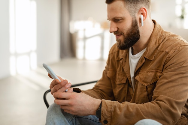 Mann mit Handy mit Ohrhörern, der drinnen Musik hört und im Internet surft